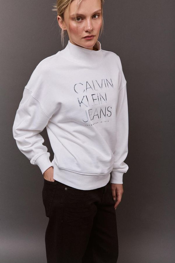 девушка в белом свитшоте Calvin Klein, серый фон
